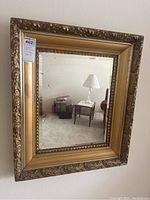 Full view of ornate antique gold gilt framed mirror showing decorative carved frame and reflection of table lamp and furniture.