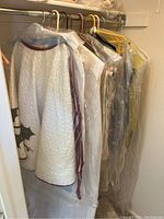 Closet rack showing hanging linens and table cloths in garment bags and plastic covers