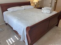 Full view of king size wooden sleigh bed with white bedding and linens stacked on top