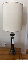 Full view of first Stiffel brass table lamp with off-white drum shade on top of wood table near wall outlet.