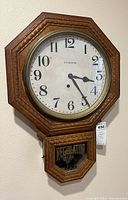 Photo of antique octagonal pressed oak wooden Ingraham regulator wall clock with white dial and 'REGULATOR' signage on lower glass panel