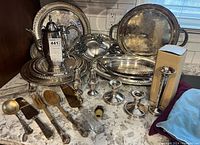 Full view of the collection showing large serving trays, pitcher, candleholders, salt and pepper shakers, and various pieces of flatware and utensils arranged on a counter.