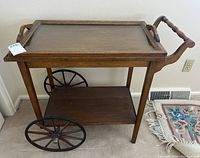 Full view of wooden tea cart showing tray top, lower shelf, large spoked wheels, and handle