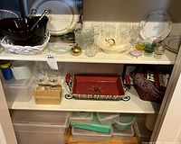 Two shelf view showing various glassware, vintage Tupperware containers, decorative plates, salad bowls, and serving trays.