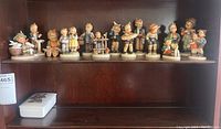 Full shelf view showing all 12 Hummel figurines and the rectangular Hummel style jewelry box on a wooden shelf.