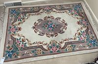 Full view of wool rug showing floral medallion center and border with fringes.