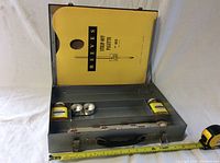 Gray metal artist paint box open with Reeves Palette booklet inside lid, showing the contents of the box including ortho linseed oil and small metal paint containers.