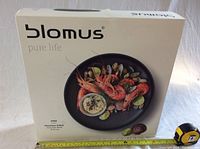 Box with Blomus branding showing a serving suggestion and mentioning 36cm cast iron bowl (Gusseisen-Schale).