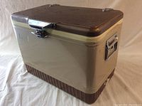 Angle view of vintage cooler showing light brown lid, beige body, brown base, chrome latch and handle.
