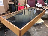 Rectangular wooden display case with a glass top resting on a table. Shows the external frame, wood finish and glass surface.