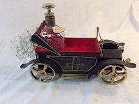 Side view of black vintage car shaped metal container holding glass decanter and shot glasses with red felt lining