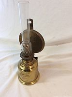 Full view of brass marine oil lamp with glass chimney and reflective back plate.