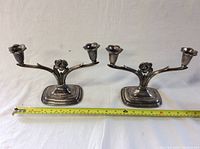 Pair of silver plate double candleholders placed side by side with a measuring tape showing width.