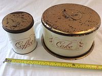 Both coffee and cake tins placed side by side with a measuring tape in front to indicate size.