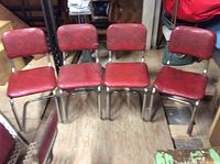 Front view of 4 red bent metal kitchen chairs in a row showing condition and style.