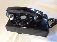 Front and side view of a black vintage rotary dial wall phone with handset and coiled cord.