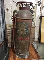 Full view of the vintage copper fire extinguisher with oxidation and patina visible on its body and handle.