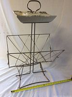 Full view of the vintage metal magazine rack with ceramic ashtray on top, showing handle and structure