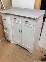 Front view of vintage white kitchen sideboard showing the Arborite top with backsplash and curved drawers on the left side with two drawers and double cabinet on the right side.