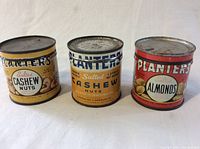 Three vintage Planters nut cans displayed upright showing front labels of salted cashew nuts and salted almonds. Used with some rust and wear.