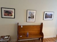 Three framed signed photographs hung on a wall above a wooden bench, showcasing different natural scenes with trees.