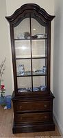 Front view of the curio cabinet showing the glass front with multiple sections and items displayed inside on glass shelves.