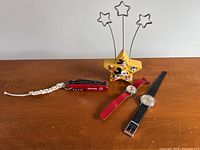 Front view of all four items: two watches, red pocket tool with lanyard, star-shaped photo holder