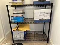 Full view of black metal wire shelving unit with some storage boxes and papers on shelves.