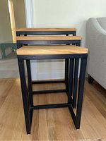 Front view of three rectangular nesting tables with natural wood tops and black metal base frames.