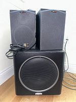 Front view of two black bookshelf speakers with gray fabric covers sitting atop a black subwoofer with a metal grille.