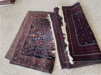 Two rugs partially rolled on carpeted floor showing pile, fringe and backing