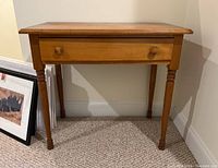 Front view of vintage wooden table with visible drawer and round wooden knobs, placed on carpeted floor against wall.