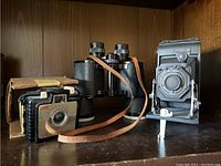 Overall lot including Kodak Brownie Bullet Camera in original box, Kodak folding camera, and black binoculars with strap