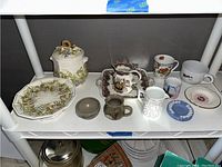 Top shelf with various assorted ceramic and ironstone items including teacups, decorative plates, mustard jar, small pitchers, and Wedgwood style plates.
