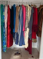 Closet view showing assortment of vintage women's clothing including coats, capes, dresses, and skirts in multiple fabrics and colors including fur