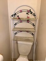 Full view of the three-tier metal shelf showing white frame, gold shelves, and pink rose decorations.