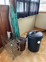 Overview of lot showing two plastic refuse bins, folded turquoise ironing board leaning against wall, vintage Hoover iron on wooden shelf, and dust pan on floor