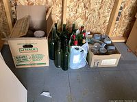 Overview of green glass wine bottles and boxes containing canning jars and miscellaneous items.