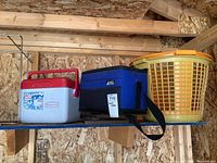 Shelf holding items including Rubbermaid cooler with red lid, Arctic Zone cooler tote, and yellow plastic basket with orange rim.