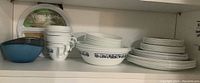 Shelving with white Corelle bowls, teacups, blue plastic bowl, and large round plastic plate