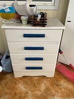 Front view of the four-drawer painted wood dresser, showing blue handles and some items placed on top.