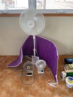 Overview photo showing the large Windmere oscillating floor fan with telescopic pole, two small desk fans (Windmere and Dayton), and rolled purple exercise mat.