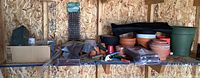 View of multiple gardening supplies on wooden shelf including planters, modular fence frames, tools, repellent mats, and metal toolbox.