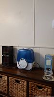 Long shot showing all items on wooden cabinet: two black MicroFurnace heaters on left, blue and white PureGuardian humidifier in center, boxed cordless electric smokeless ashtray, and two clear glass ashtrays on right.