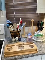 Full countertop view showing decorative utensil holder with kitchen utensils, wooden holders for paper towel and bananas, salt and pepper shakers, and disposable plates and cutlery.