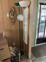 Photo showing two floor lamps side by side against a wood-paneled wall. One lamp is white, the other green. Both lamps approx 70 inches tall, multiple light fixtures visible.