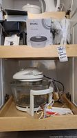 Shelf with Rival branded box for 6-cup rice cooker and Rival 6-cup rice cooker appliance with glass bowl, lid, heating base, and cord