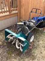 Full side view of the snow blower showing handle, engine, tires, and 29-inch green metal auger housing with white blades.