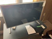 LG 32-inch LED TV on a black table, accompanied by remote control and manual.
