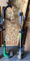 Photo showing two edge trimmers standing upright against a wood wall, one green corded Weed Eater and one gray/green Earthwise cordless model.